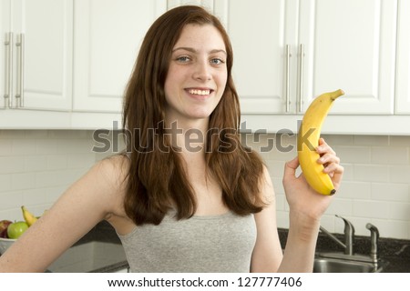 Young woman holds banana  which has a low glycemic index or  low GI  in kitchen with white cabinets