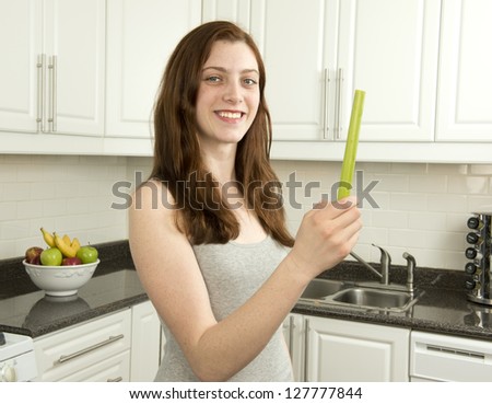 Young woman holds  celery  which has a low glycemic index or  low GI  in kitchen with white cabinets