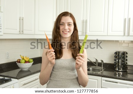 Young woman holds  carrot and celery which has a low glycemic index or  low GI  in kitchen with white cabinets