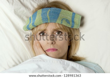 Woman sick in bed or hospital with washcloth on face