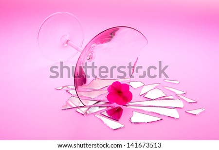 Concept photo of broken relationship with flower sitting in broken martini glass shot on light table with red  light