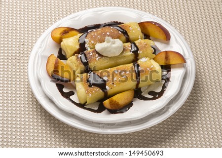 Traditional Jewish food cheese blitzes with whipped cream, peaches and chocolate sauce