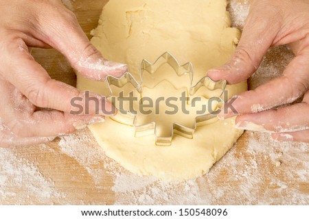 Hands pushing Canadian maple leaf shaped cookie cutter into dough shot from above