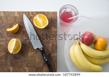 Arrangement of fruit: apples, oranges sliced on cutting board , bananas and a red fruit drink in breakfast setting shot from above