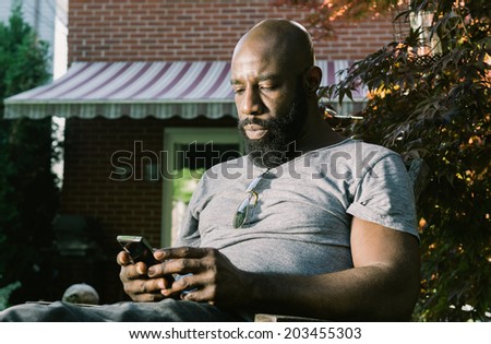 African American man reacts as he reads and email or text message while enjoying a glass for red wine in the backyard garden