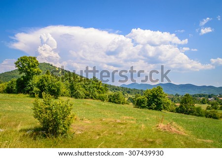 Meadow hillside mountain landscape with strong powerful white clouds climbing up from the top of the hill, and mountains in the background. Velebit mountain, Croatia