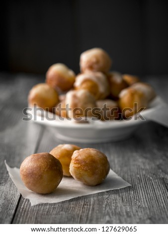 Small homemade doughnuts, also known as doughnut holes, prepared for Polish Fat Thursday. On the foreground three doughnuts on a piece of baking paper, in the background a white bowl full of doughnuts