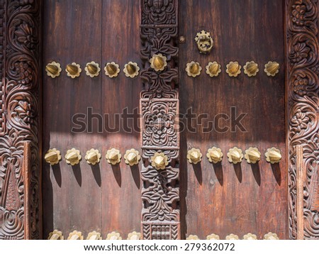 Horizontal photo of an old traditional wooden carved door in Stone Town, Zanzibar, Tanzania, East Africa, with typical metal elements and carved floral ornaments.