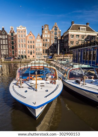 AMSTERDAM, NETHERLANDS - JUNE 15, 2015: Cruise tourist boat on a Damrak canal in Amsterdam, Netherlands, on a summer day. Traditional houses in the background.