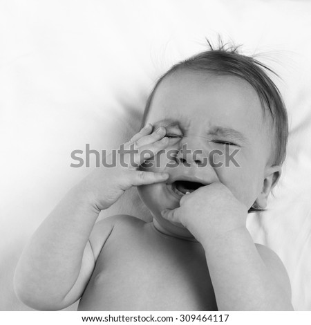 baby lying on a white pillow and crying teething
