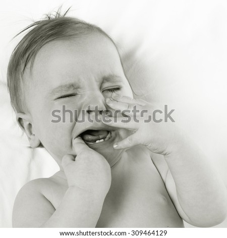 baby lying on a white pillow and crying teething