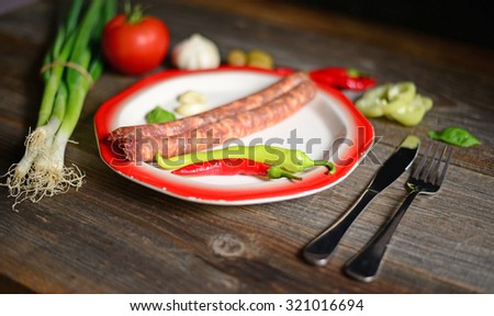 Portion of sausages on plate with tomatoe, fresh onion, chilly peppers and olives on wooden background
