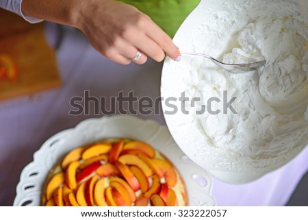 Woman hand put whipped cream on peach cake