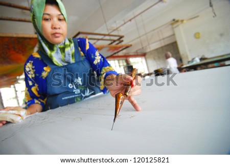 KUALA TERENGGANU ,TERENGGANU - JAN 11 : An artist carefully trace the floral motif on a traditional batik fabric using melted wax on January 11, 2009, Kuala Terengganu, Malaysia