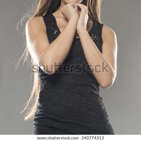 close up of beautiful sexy girl with praying hands. wearing black dress. isolated on gray studio background.