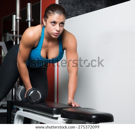 Sporty girl doing exercise with dumbbell in fitness hall. Attractive fitness woman, trained female body, lifestyle portrait, caucasian model. Fitness theme.