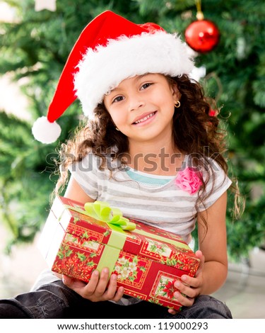 Little girl sitting by the tree holding a Christmas gift