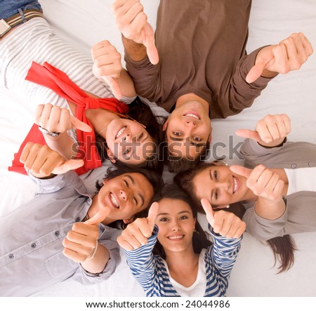Group of friends with their heads together on the floor with thumbs up - isolated