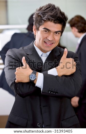 Young business man in an office with both thumbs up