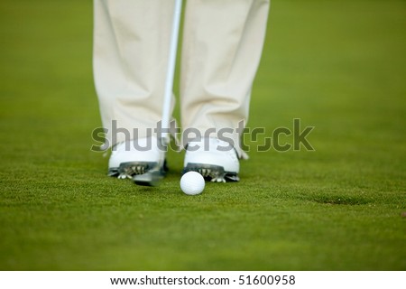Person\'s feet playing golf with the ball near the hole