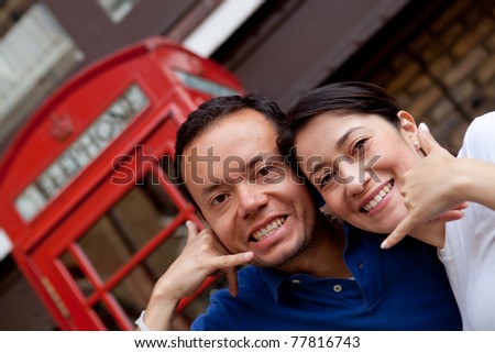 Couple standing in front of a telephone box in London doing a call me gesture