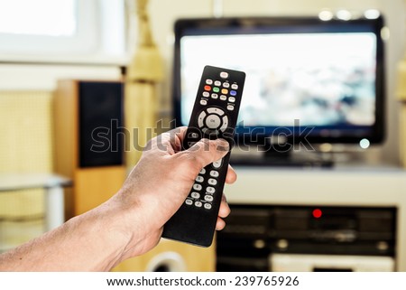 Men\'s hand sends the remote control on the TV in the living room