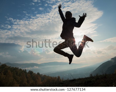 Silhouette of happy young woman jumping at the sunset