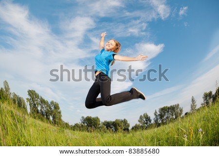 Happy girl jumps against a green grass and the blue sky