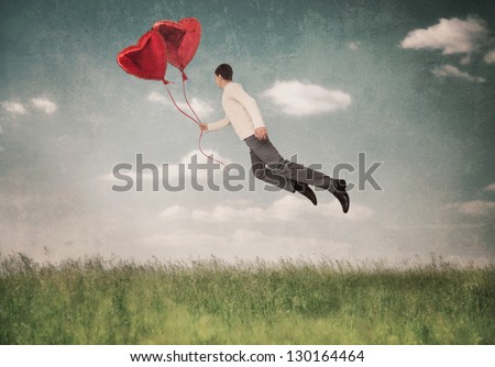 The young  man flying by a balloon in the form of heart
