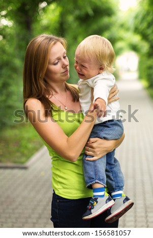 Portrait of a crying little boy who is being held by her mother , outdoors
