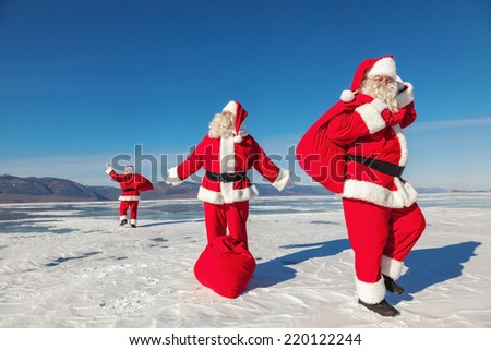 Three Santa Claus with a bag of gifts in different directions on the ice in winter, multiexposition, shooting was conducted in a sunny day on lake Baikal