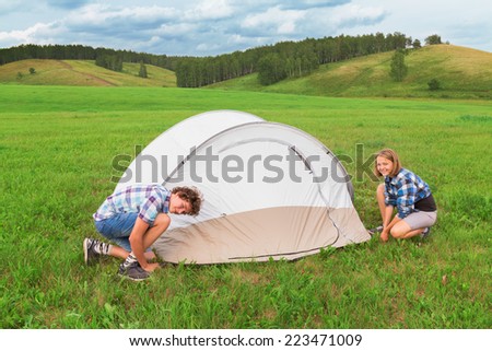 Teenage boy and girl arranges tourist tent on green grass