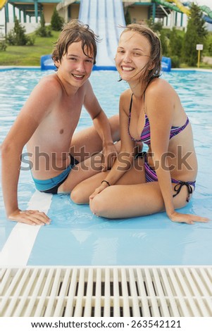 Happy teenage boy and girl sitting on the edge of the pool water park