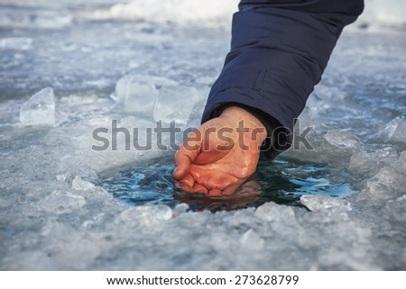 Male hand scoops water from the hole of the Lake Baikal