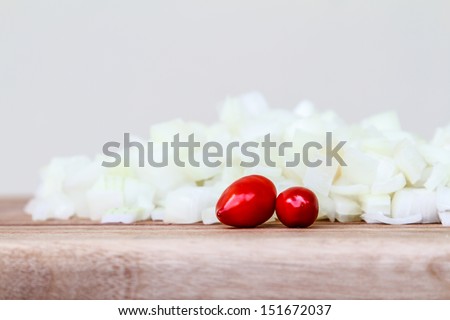 Pile of Diced White Onion and Chillis.  Side view of freshly chopped white onion, garnished with two fresh red chilies, on a wooden chopping board
