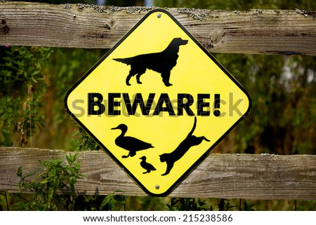 Beware. Unusual mix of animals on this fluorescent road sign. Diamond shape sign on a rustic fence.