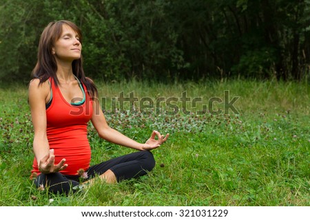 a pregnant woman sitting cross-legged on the grass