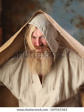 Portrait old beggar with a beard and mustache, wrapped in burlap, with pain and despair in his eyes, the studio on a brown-blue background