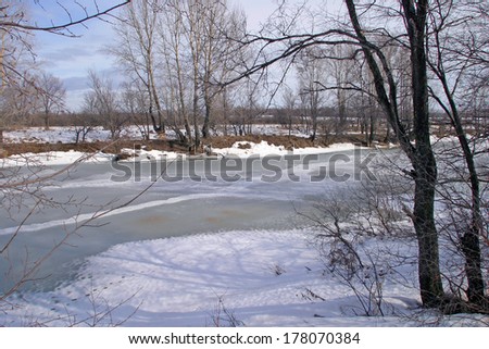 picturesque spring landscape with river ice melted bare trees and beautiful clouds in the blue sky