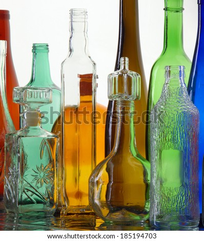 close-up clean transparent colored glass bottles of different shapes on the mirror surface in white light studio