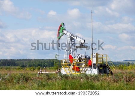 summer landscape oil pump in a green field, cloudy sky above him and the forest on the horizon