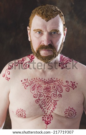 close-up portrait of an adult male with a naked torso and body painting with henna and colored hair and beard studio