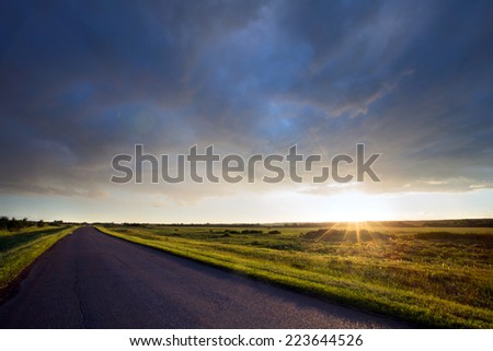 summer landscape road to the horizon at sunset and dramatic clouds on a blue sky