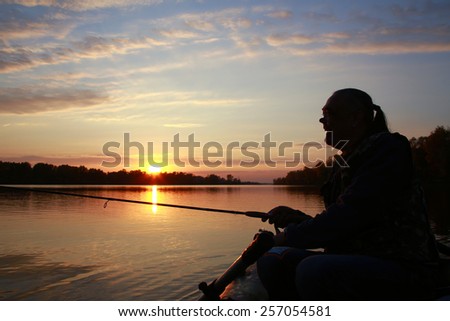 Portrait of a man in profile in a boat on a river with a fishing pole in his hands at sunset in autumn