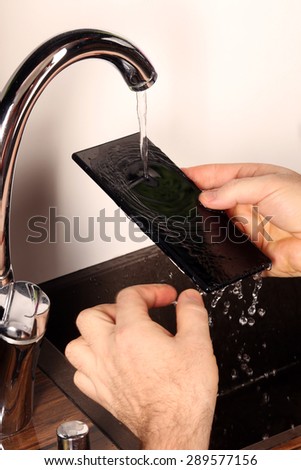 close-up smartphone under the tap water in male hands
