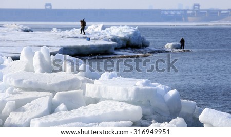 landscape Fishermen catch fish on the ice of a large reservoir in the early spring ice drift