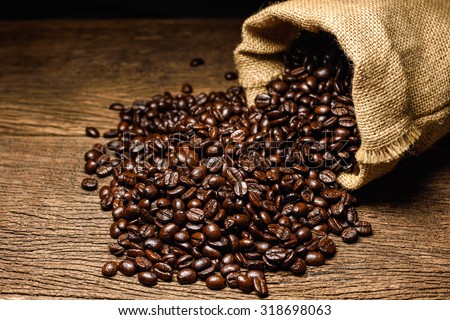 Coffee beans in coffee burlap bag on wooden surface.