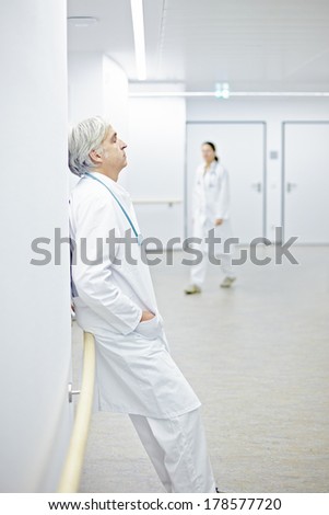 Tired doctor leaning against wall in hospital