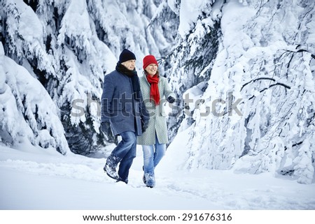 Couple walking in the snow in front of a snowy forest with fir trees