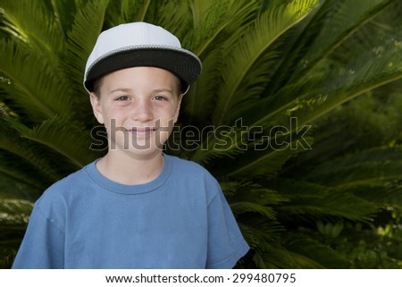 Boy wearing baseball hat standing by palm